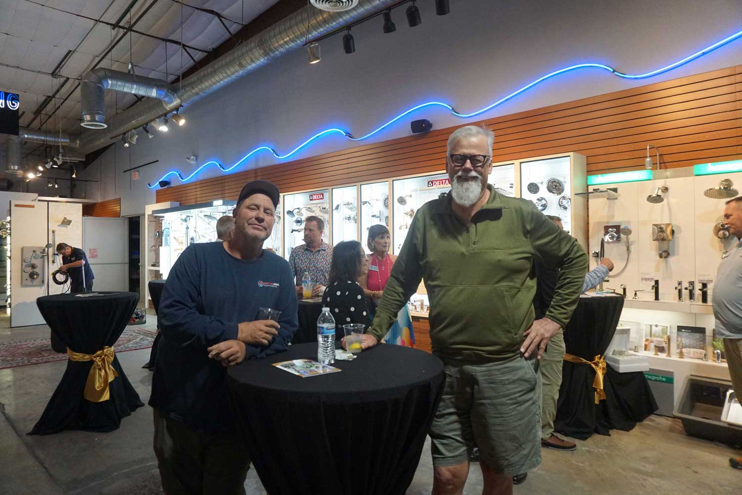 Two men leaning on a cocktail table in front of a Delta display wall.