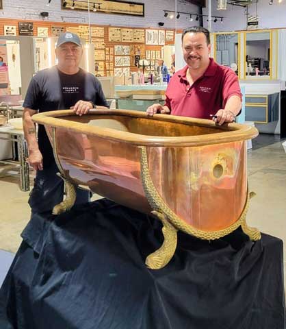 Two men standing behind a large copper bathtub display in the showroom.