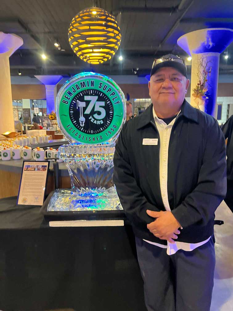 Man smiling while standing next to the Benjamin Supply 75th Anniversary ice sculpture.