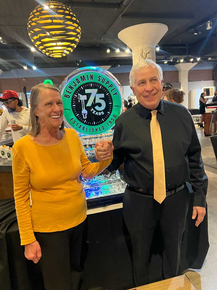 Older couple holding hands and smiling next to the anniversary ice sculpture.