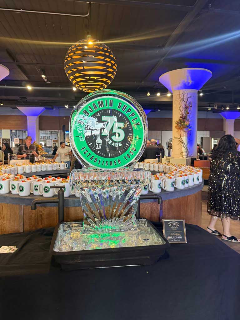 Lighted ice sculpture with anniversary mugs in the background.