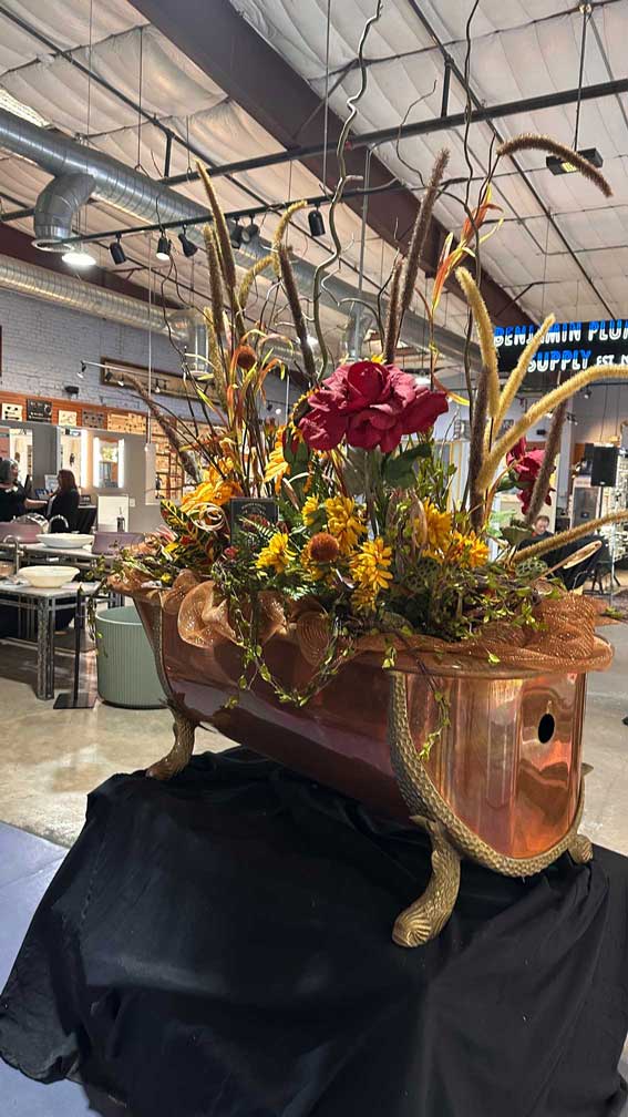 Large copper bathtub filled with an elaborate autumn floral arrangement with sunflowers.