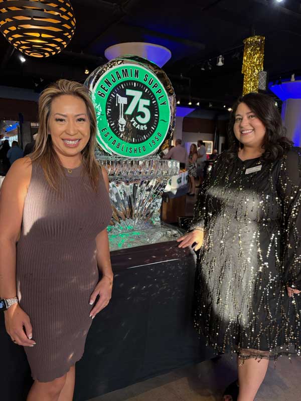 Two women in evening wear posing next to the lighted 75th Anniversary ice sculpture.