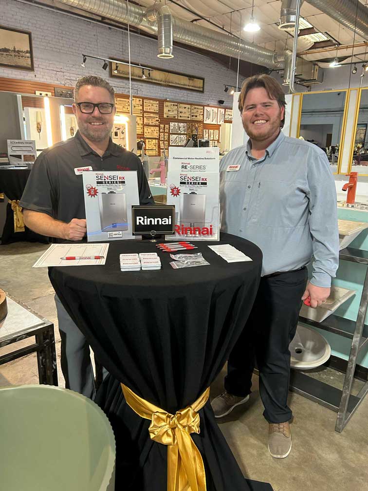 Two men standing at a table displaying Rinnai tankless water heaters brochures.
