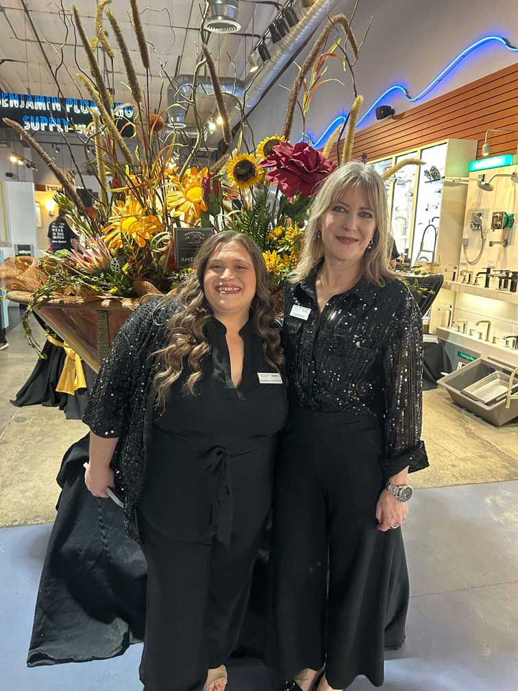 Two women posing next to a large floral arrangement in a copper tub.
