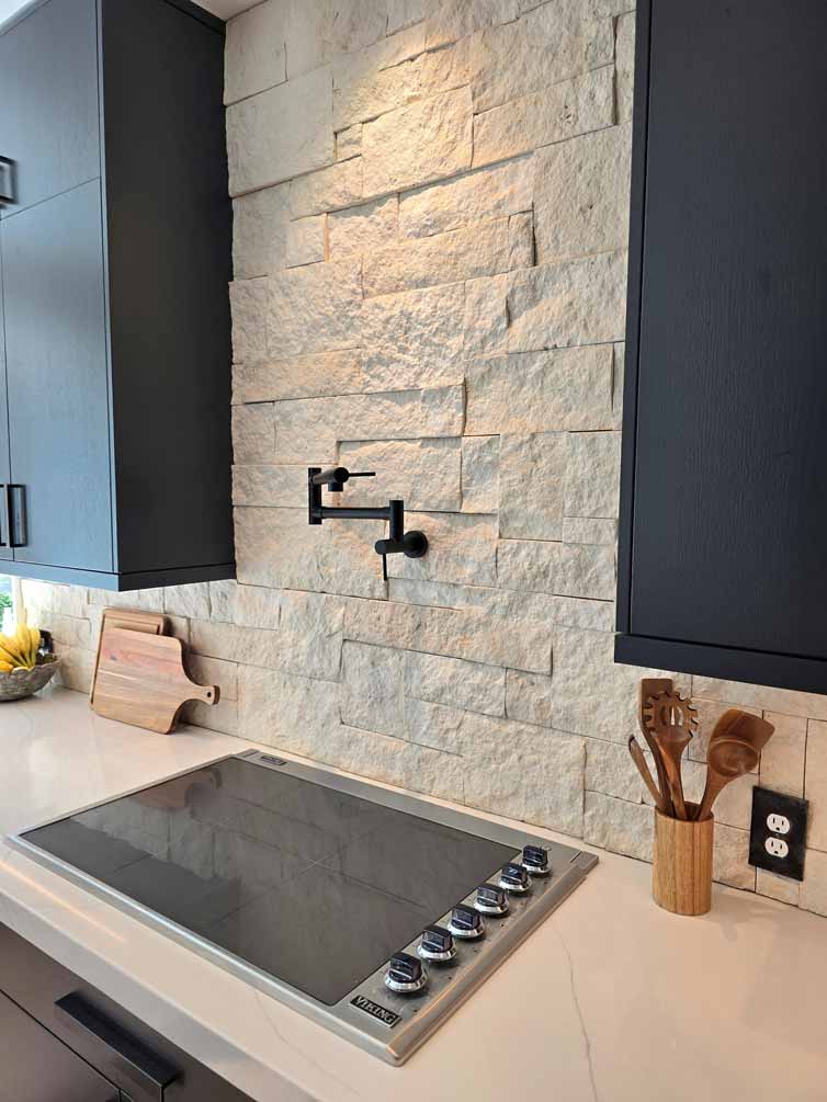 Modern electric cooktop installed on a quartz countertop with textured stone backsplash and black pot filler