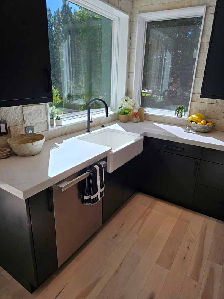 Corner view of kitchen sink area with white farmhouse sink, black faucet, and surrounding windows with natural light