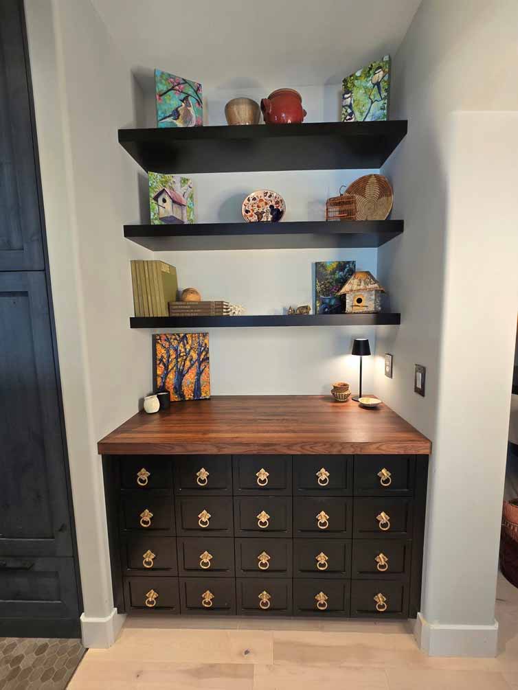 Decorative nook with black drawers featuring brass ring pulls, floating shelves, and colorful art pieces