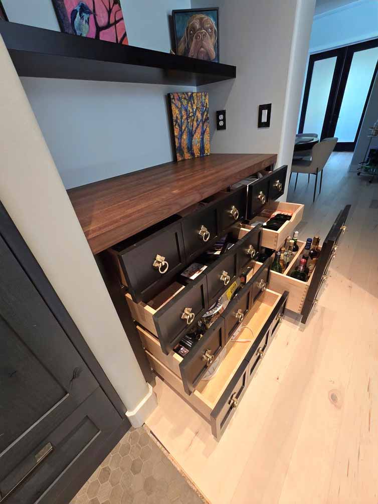 Open drawers in a decorative kitchen storage unit, revealing neatly organized snacks, utensils, and bottles