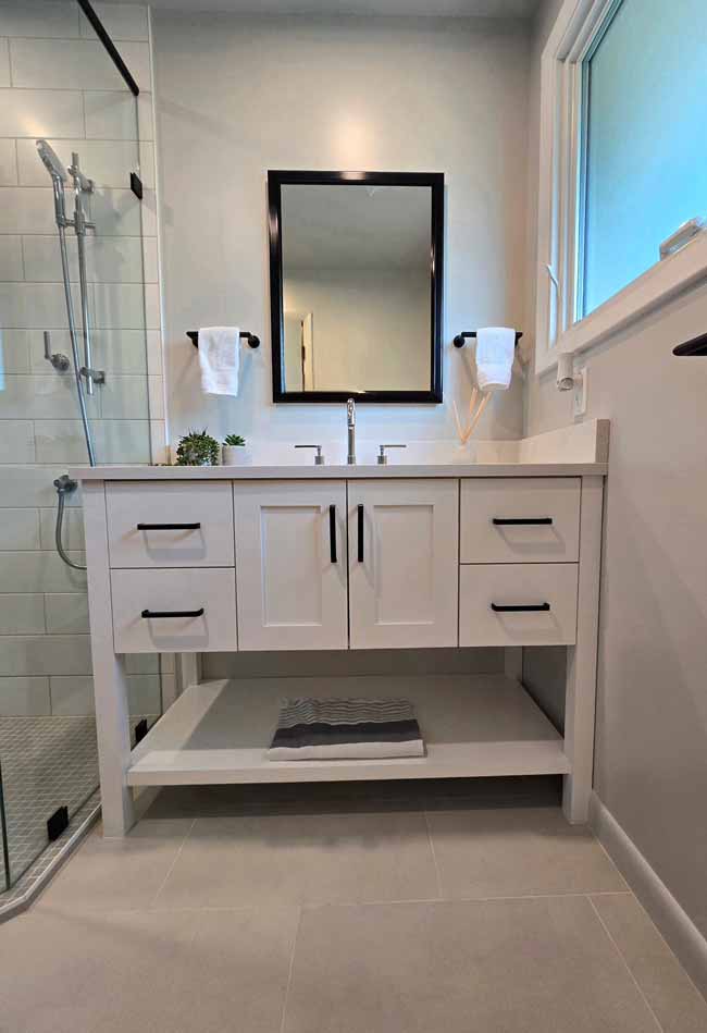 Modern bathroom vanity with white cabinets, black hardware, and a large mirror above a quartz countertop