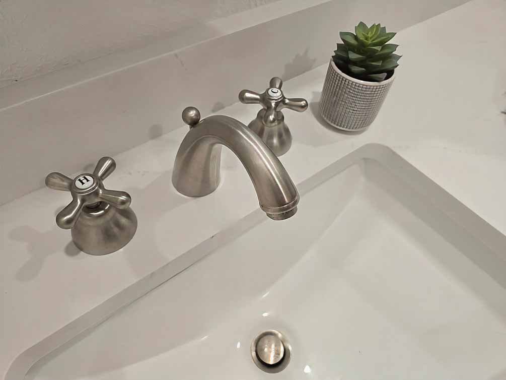 Close-up of brushed nickel faucet with hot and cold cross handles on a white bathroom sink with a small potted plant