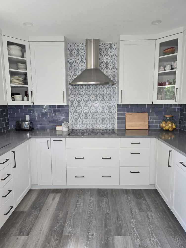 Contemporary white kitchen with patterned backsplash, dark gray countertops, and a stainless steel range hood