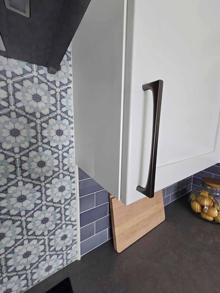 Detail view of white kitchen cabinet with modern black handle next to a patterned tile backsplash