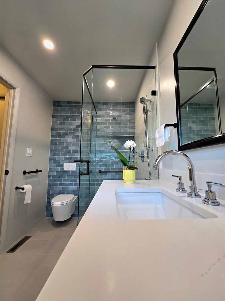 Modern bathroom with floating vanity, glass shower enclosure, and blue subway tile accent wall