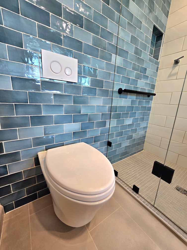 Wall-mounted toilet next to a glass shower with blue subway tiles and black grab bar