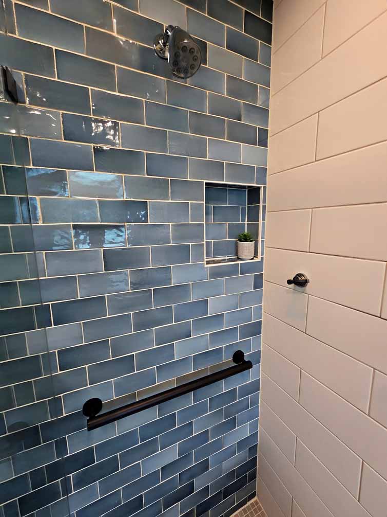 Blue tiled shower with built-in shelf, black grab bar, and chrome showerhead