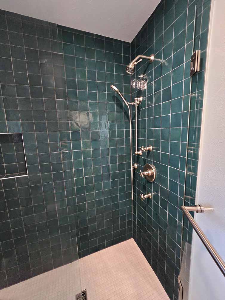 Shower with dark green square tile walls, multiple chrome showerheads, and built-in shelf