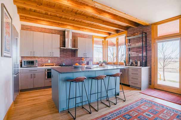 Warm modern kitchen with brick backsplash, exposed wood beams, and blue island with barstools