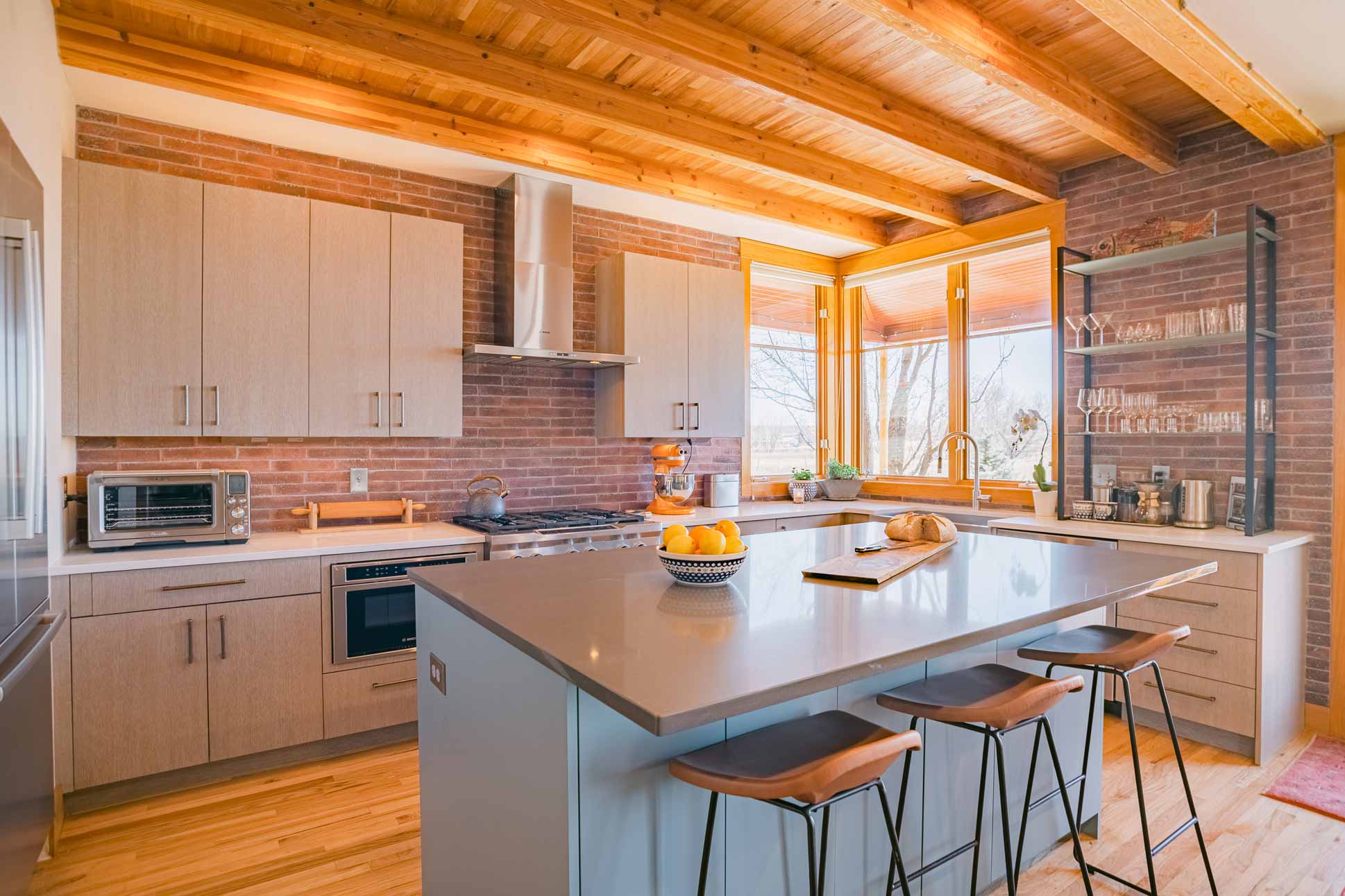 Wide view of kitchen with wood ceiling beams, gray countertops, brick walls, and stainless steel appliances