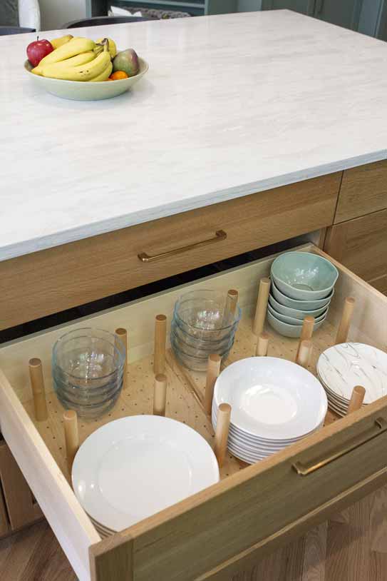 Open kitchen drawer with wooden peg system organizing plates and bowls beneath a white countertop