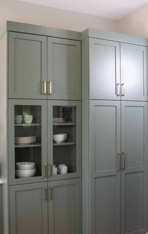 Tall sage green kitchen cabinets with glass doors displaying neatly stacked dishes and bowls