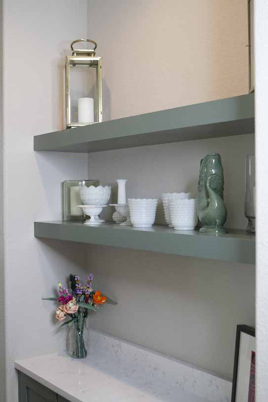Decorative nook with sage green floating shelves holding white glassware and ceramics above a marble countertop