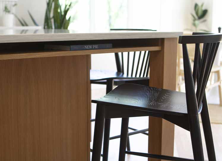 Close-up of black spindle-back barstools tucked under a light wood island with a cookbook shelf labeled "New Pie"