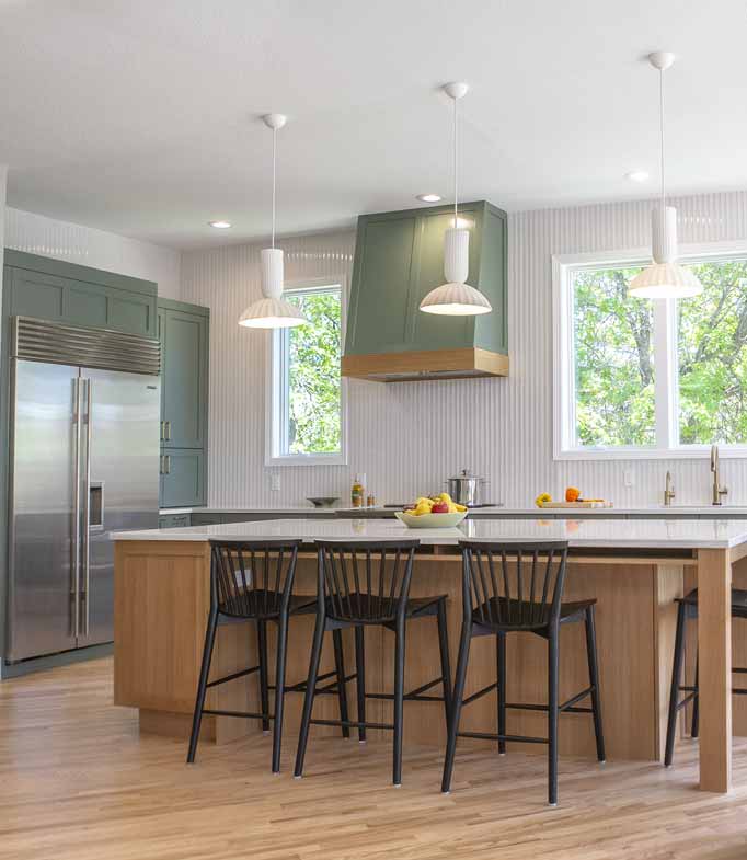 Modern kitchen with large island, sage green cabinets, pendant lighting, and built-in stainless steel fridge