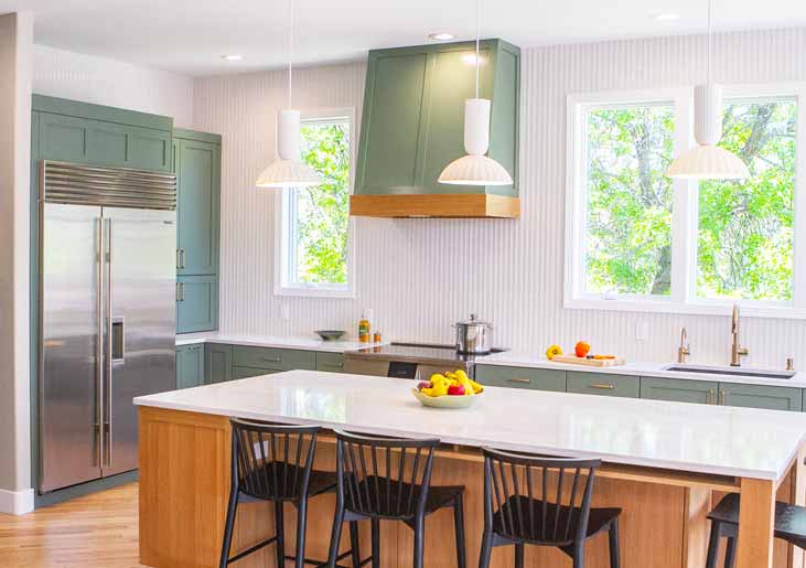 Bright kitchen with sage green cabinetry, wood range hood, and white island under three pendant lights
