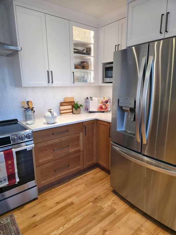Modern kitchen with white upper cabinets, wooden lower cabinets, white countertops, stainless steel appliances including refrigerator and stove, and hardwood flooring.