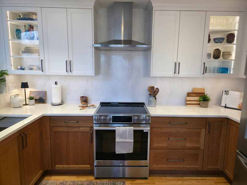 U-shaped kitchen with two-tone cabinetry featuring white upper cabinets and wooden lower cabinets, stainless steel range with hood, white countertops, and built-in display shelving with lighting.