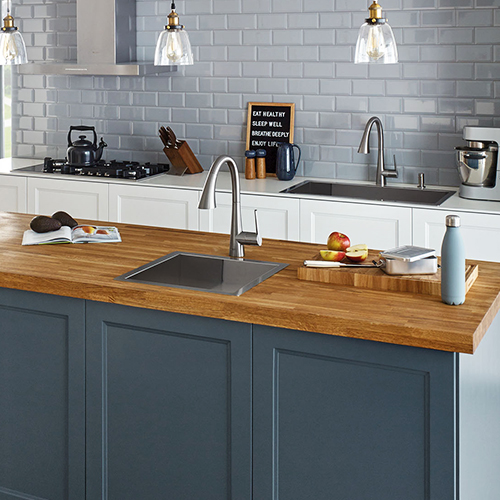 Cuisine complète suivant la tendance de deux éviers dont un évier de bar sur l’îlot central avec robinet de bar ainsi qu’un évier sur le plan de travail avec un robinet et distributeur de savon au fini chrome de la collection Zedra de Grohe