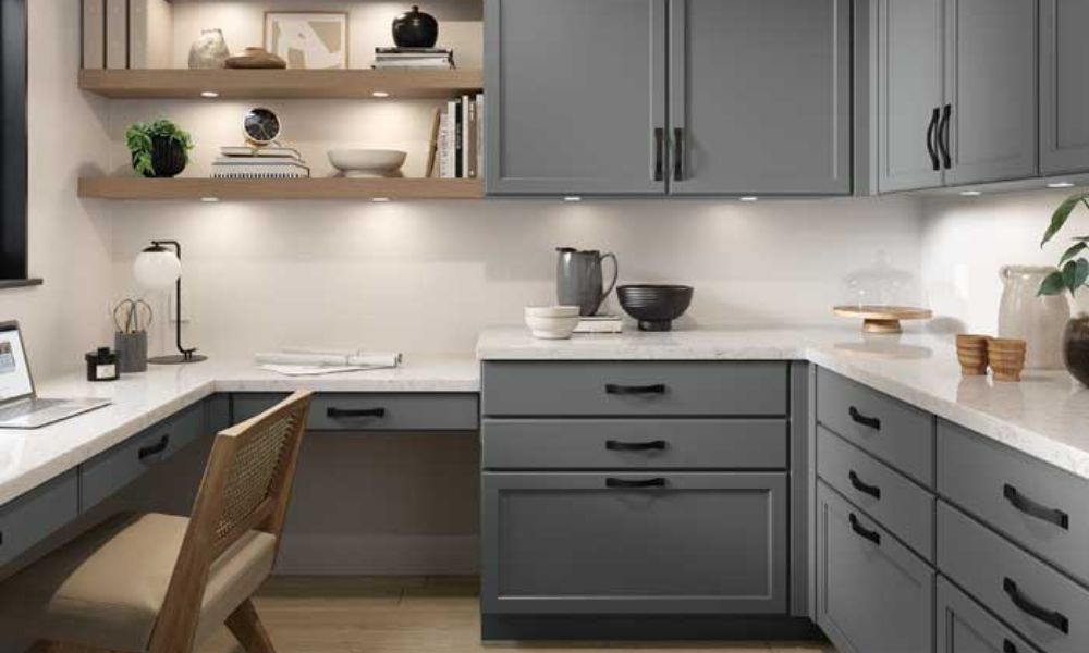 A sleek home office with gray shaker cabinets, a white countertop serving as a desk, and floating wood shelves with integrated lighting.