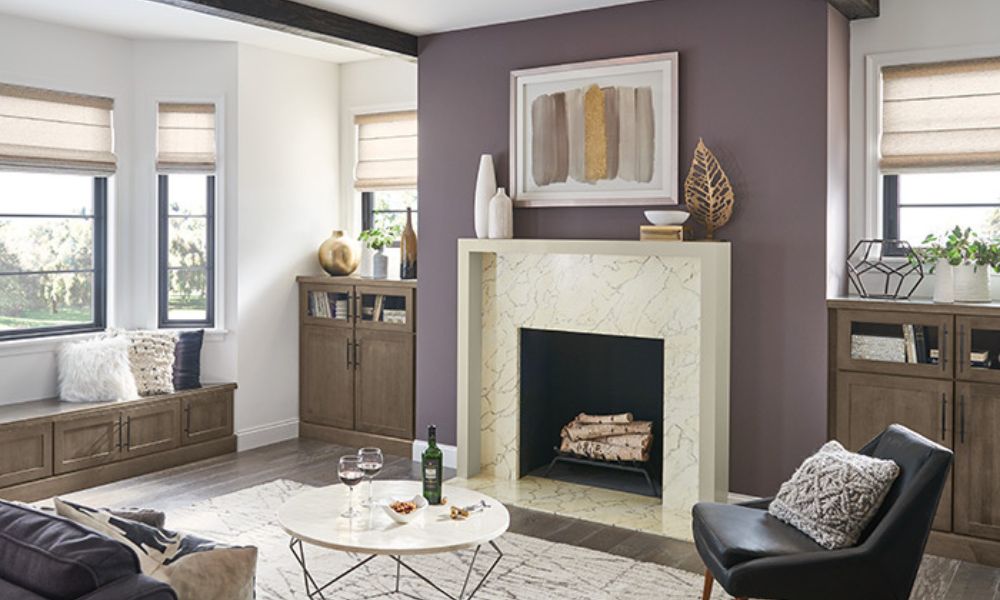 A stylish living room with a prominent purple accent wall, a modern white marble fireplace, and surrounding built-in cabinets in a warm, light wood finish.