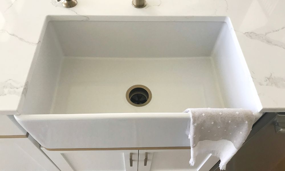 A white sink with a towel hanging from the faucet, set against a neutral background.