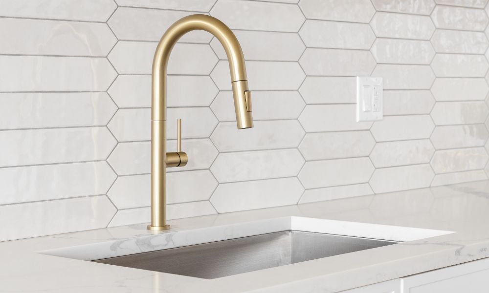 A modern kitchen featuring a gold sink and white tiled walls, showcasing a sleek and stylish design.