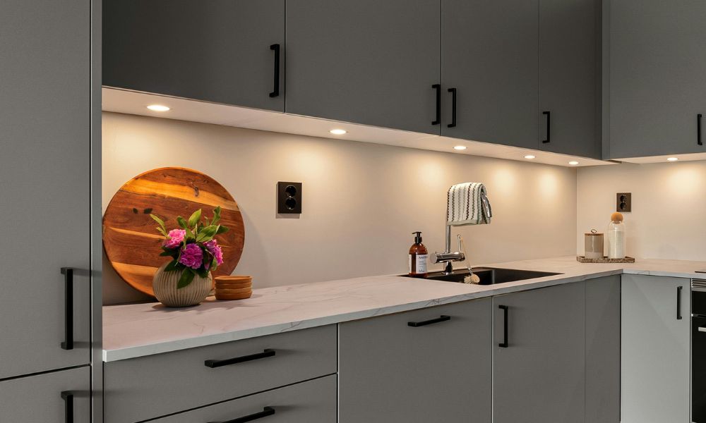 A modern kitchen featuring grey cabinets and sleek black countertops.