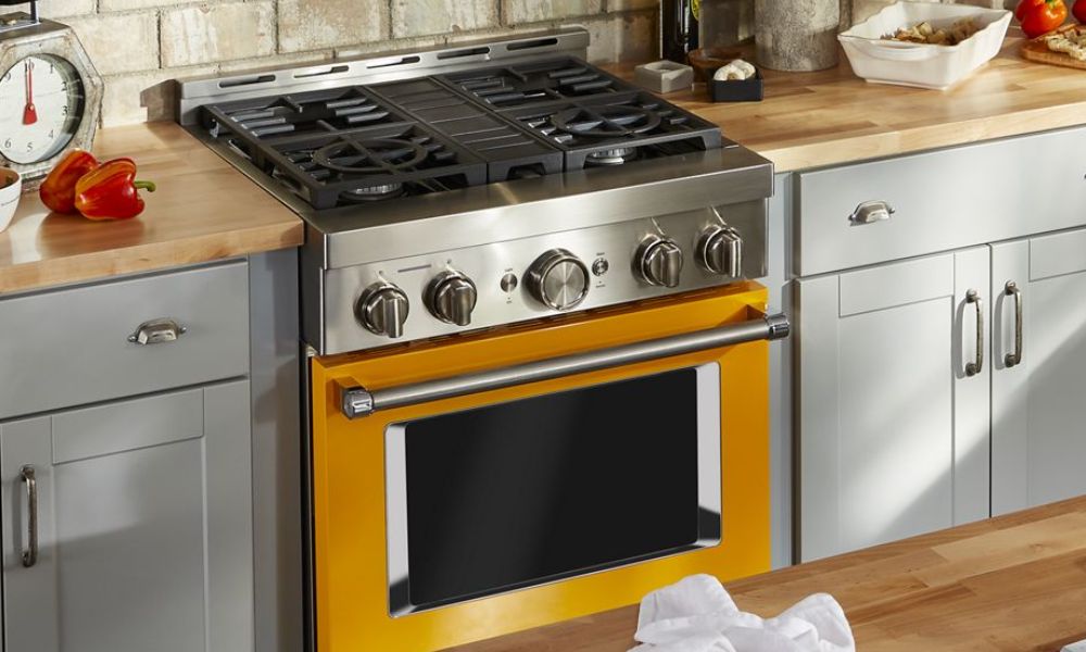 A kitchen featuring a bright yellow stove top oven, surrounded by modern cabinetry and kitchen essentials.