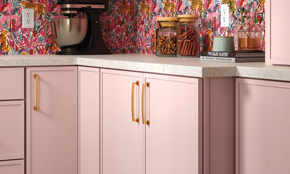 A pink kitchen featuring floral wallpaper and elegant gold hardware accents.