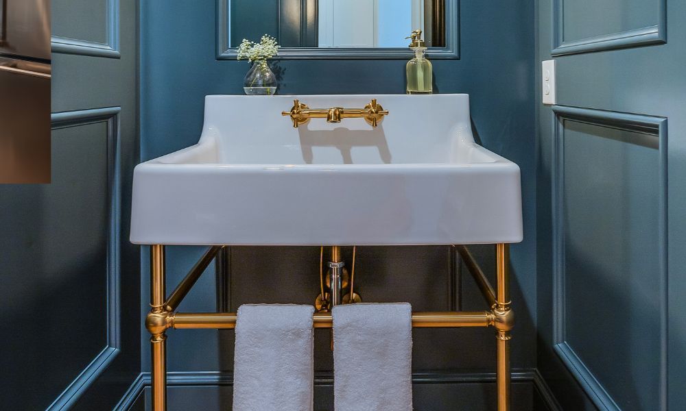 "White lavatory console sink with brass legs against a dark blue wall