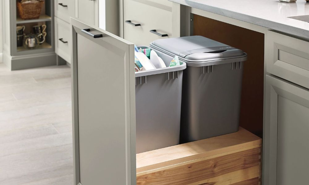 A base cabinet pulled open to reveal two grey waste bins stored in a wooden frame