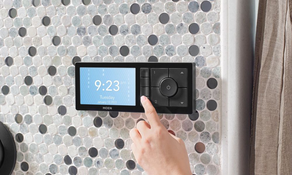 A hand using a digital smart shower control panel from Moen.
