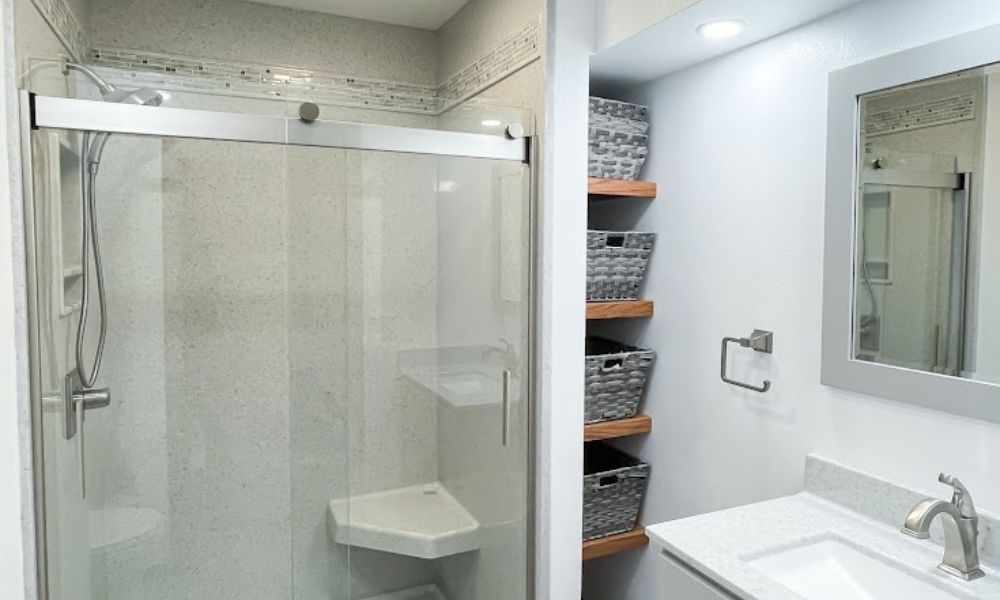 A basement bathroom with a glass sliding-door shower, built-in corner shower seat, and wall-mounted woven storage baskets on wooden shelves above the vanity