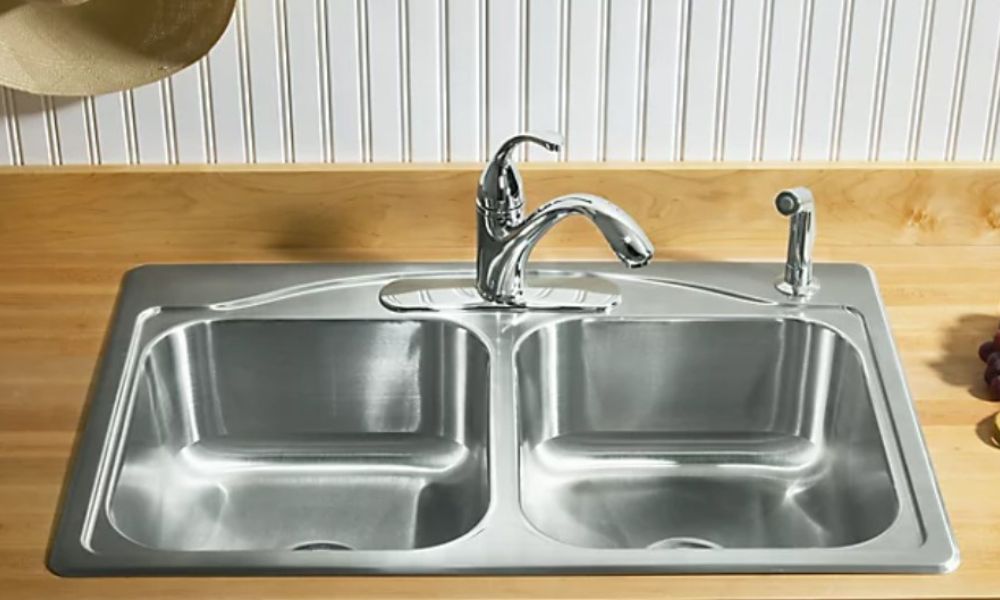 A stainless steel kitchen sink featuring two separate faucets for hot and cold water.